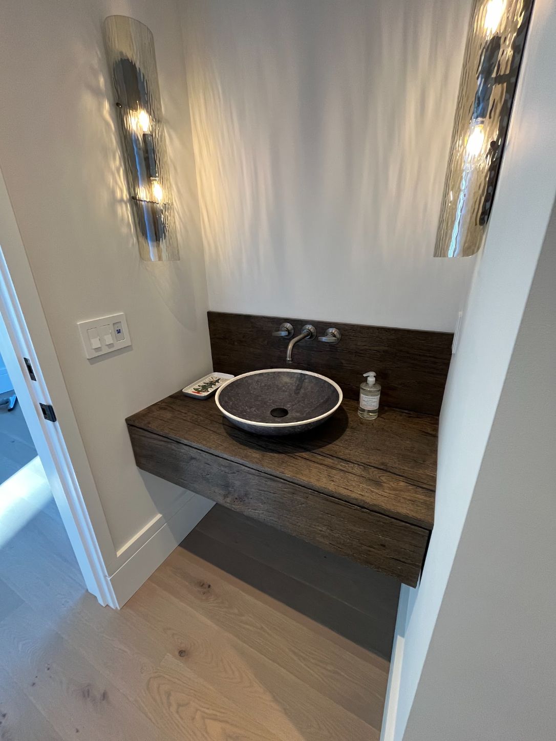 Floating walnut powder room vanity with a black vessel sink between two wall sconces