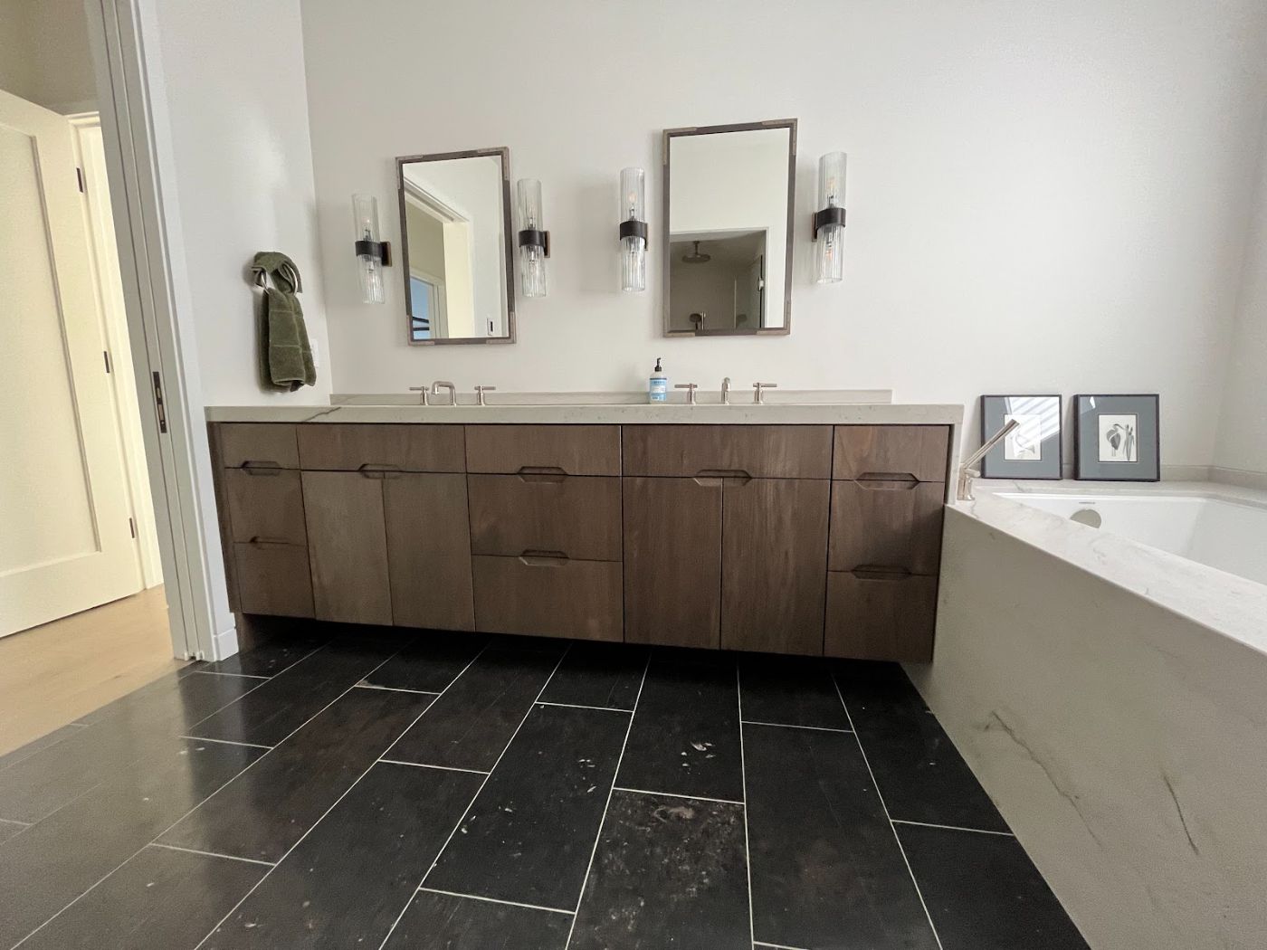 Walnut double vanity with a white stone top, two sinks and twin mirrors over a black slate tile floor
