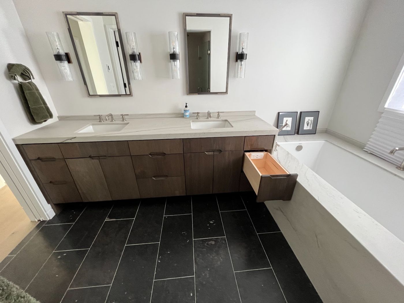 Walnut double vanity with one drawer pulled out, beside a tiled tub