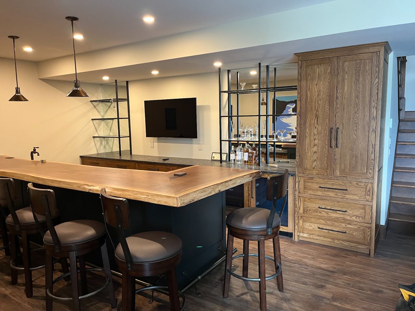 Basement bar with a live-edge wood counter on a navy base, bar stools and a tall wood storage cabinet