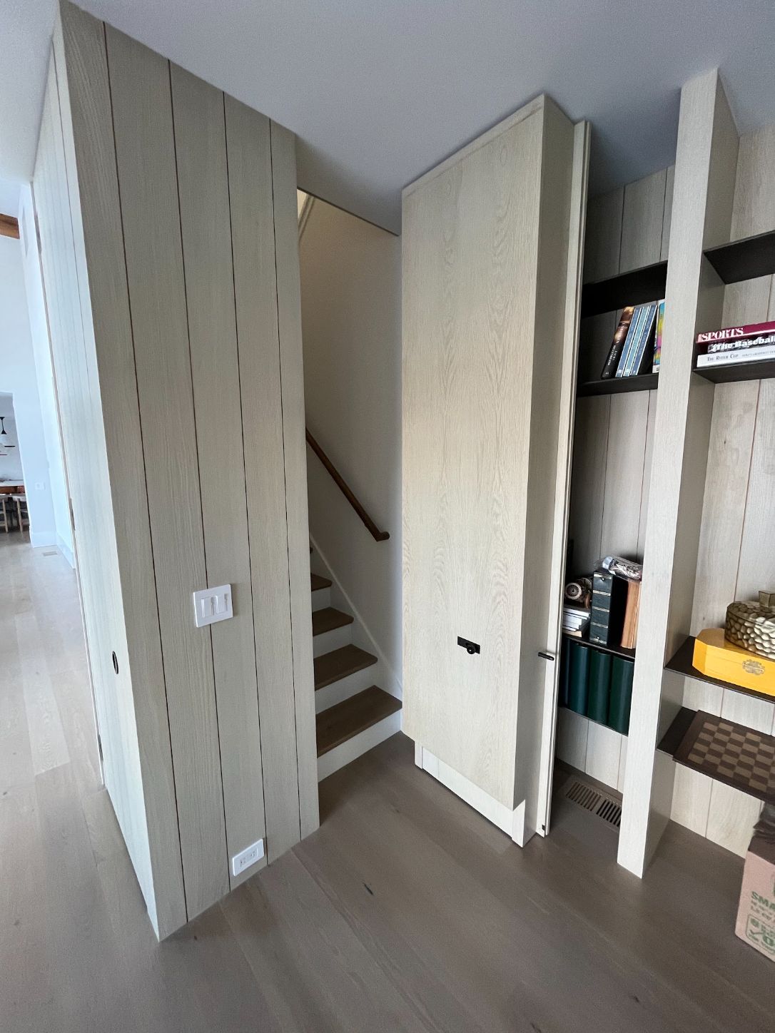 Paneled hidden bookcase door swung open onto a staircase, with open shelving built into the wall beside it