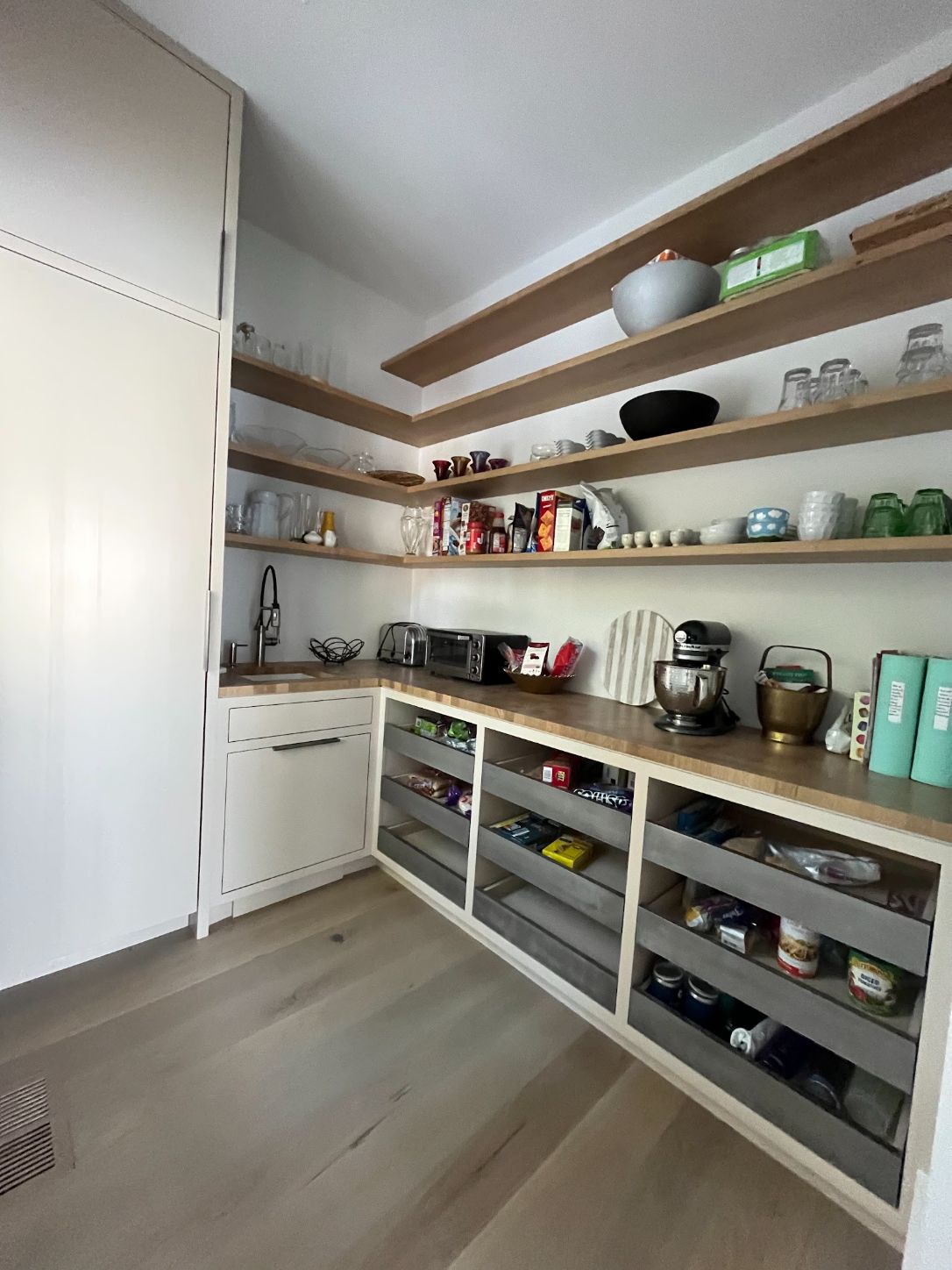 Walk-in pantry with open wood shelving over a counter and pull-out bins below
