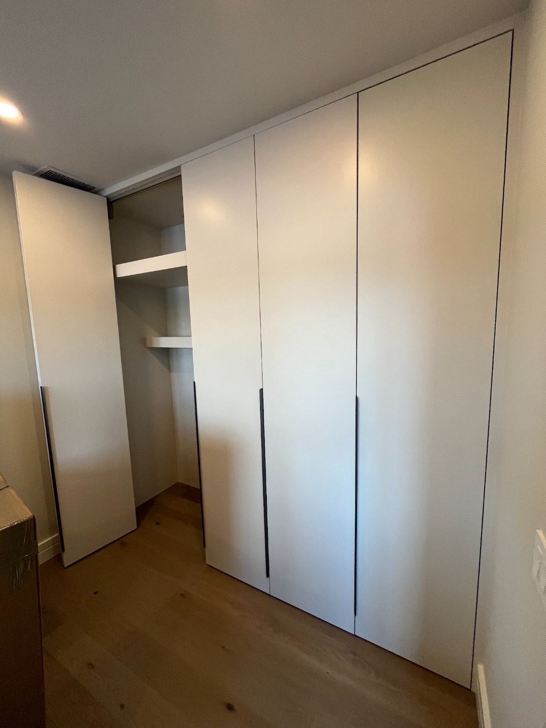 Floor-to-ceiling built-in wardrobe with white flat-panel doors, recessed finger pulls and open shelving at one end