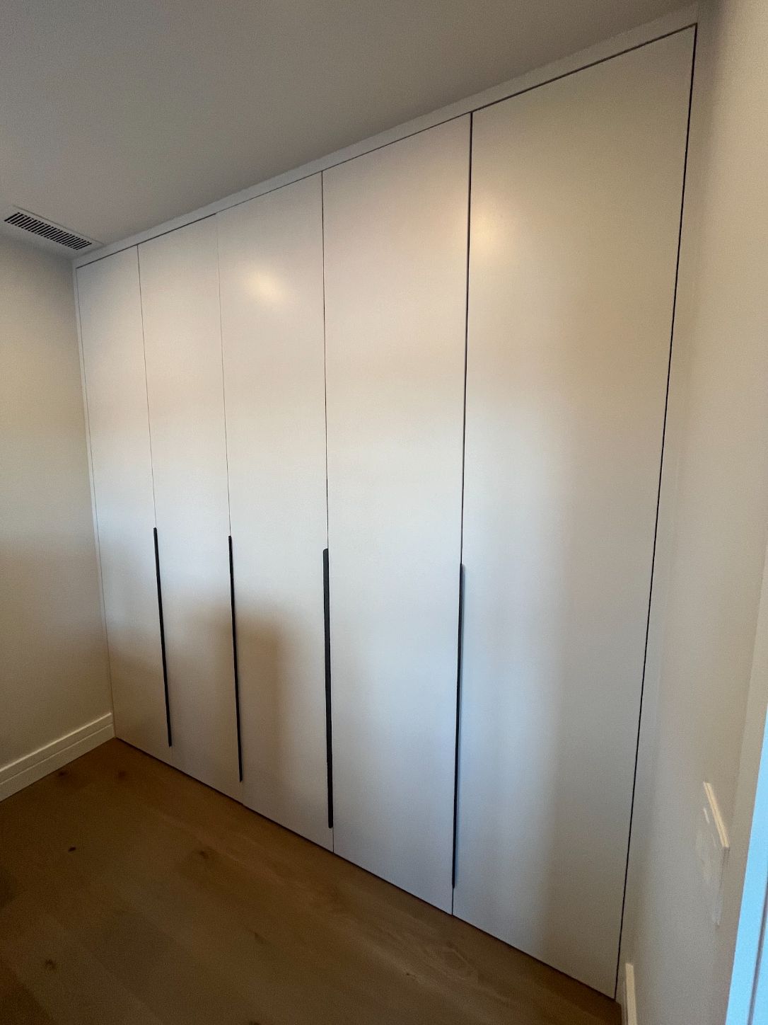 Wall of floor-to-ceiling white built-in wardrobe doors with recessed finger pulls