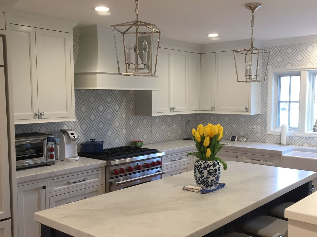 Classic white kitchen with marble countertops, patterned backsplash and lantern pendants