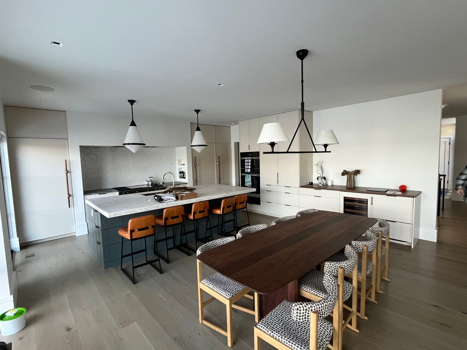 Modern kitchen with handleless white cabinetry, a deep teal island under a marble top, walnut counter run and integrated wine storage
